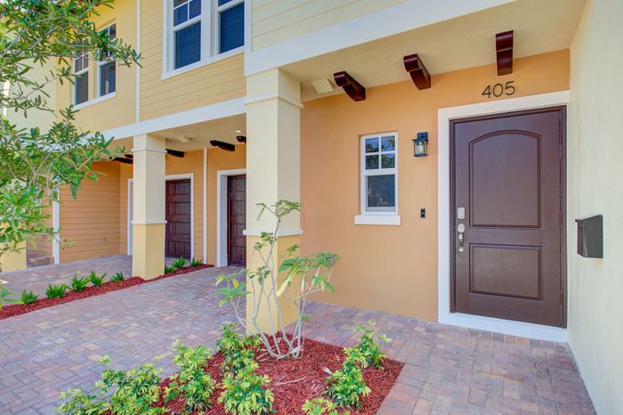 Charming townhouse entrance with elegant wooden door, inviting brick pathway, and lush greenery for a warm welcome.