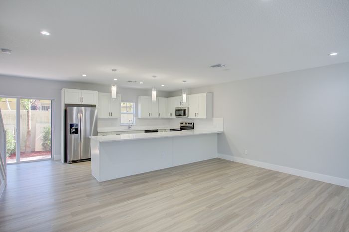 Modern open-plan kitchen with sleek white cabinetry, stainless steel appliances, and large island, complemented by elegant pendant lighting and expansive wood flooring.