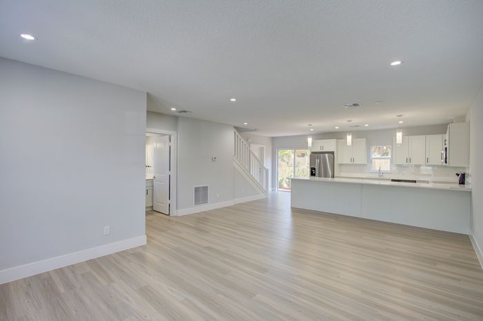 Bright and spacious open-concept living area featuring elegant wood flooring, modern kitchen with sleek white cabinetry, and ample natural light.