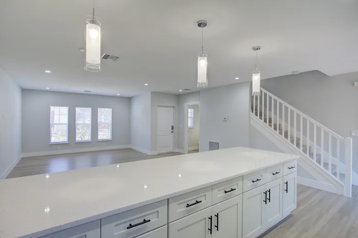 Modern open-concept living area with sleek kitchen island, elegant pendant lighting, and inviting staircase leading to upper level.