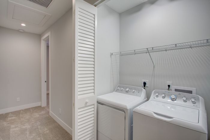 Modern laundry area featuring sleek white washer and dryer units, ample shelving space, and elegant louvered doors.