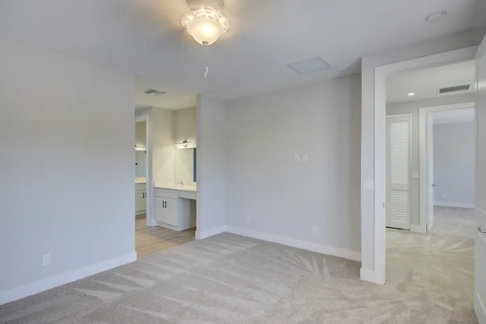 Bright and inviting bedroom with plush carpeting, modern ceiling fan, and sleek bathroom vanity, perfect for luxury living.