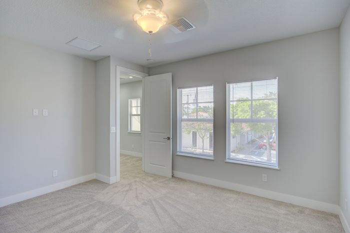 Bright, airy bedroom with plush carpet and large windows letting in natural light, offering a serene view.