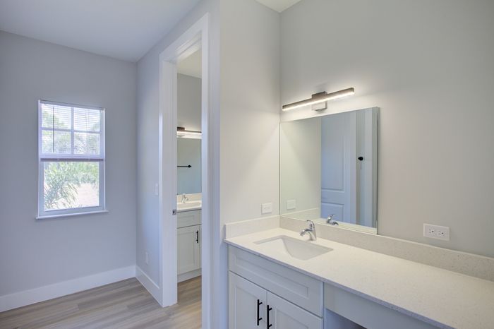 Bright and modern bathroom with sleek white cabinetry, elegant vanity mirror, and abundant natural light from a large window.