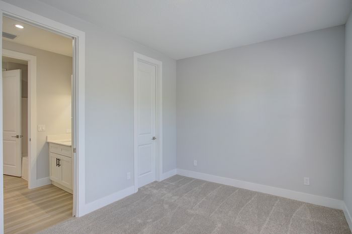 Bright and airy unfurnished room with plush new carpeting and freshly painted walls, connected to a sleek bathroom with modern fixtures.