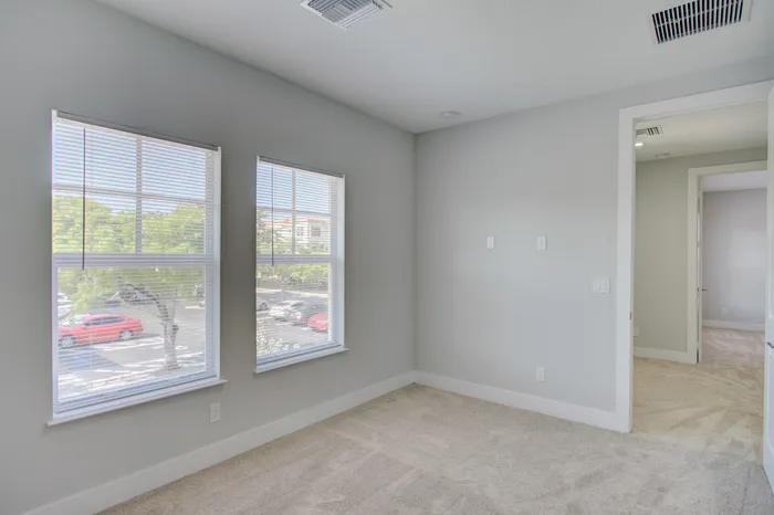 Bright and airy room with plush carpet, large windows, and fresh neutral decor, perfect for a cozy setup.