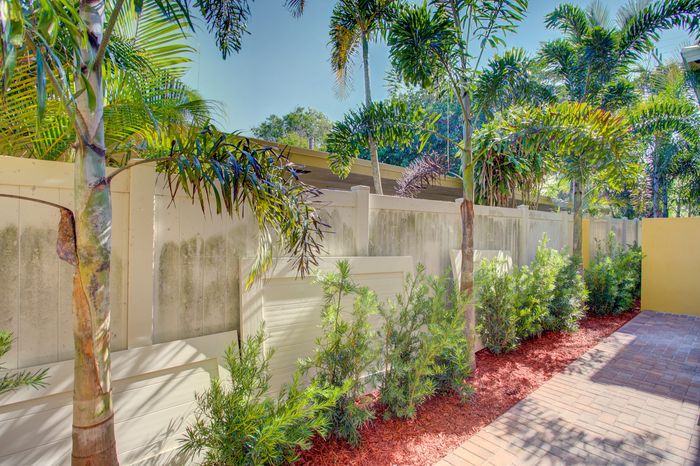 Inviting outdoor space featuring lush palm trees and vibrant greenery against a backdrop of a stylish white fence.