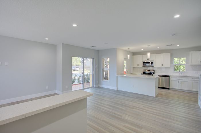 Elegant open-concept living room and kitchen with sleek white cabinetry, modern appliances, and abundant natural light.