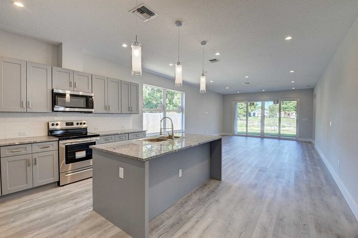 Modern open-plan kitchen and living area with sleek grey cabinetry, island with granite countertop, and large windows offering abundant natural light.