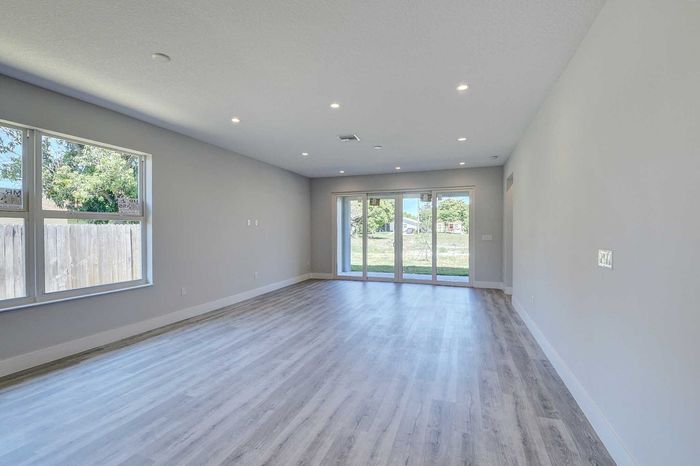 Bright and airy living area featuring modern wood flooring, large windows, and patio doors with a clear garden view, designed for comfortable and stylish living.