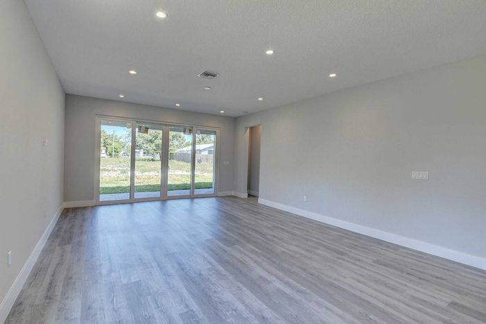 Bright, spacious living room with elegant wood flooring and large glass doors opening to a serene outdoor view.