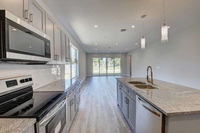 Modern kitchen with sleek stainless steel appliances, granite countertops, and spacious open layout leading to bright living area with large windows.