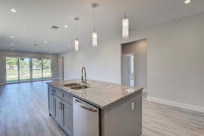 Bright contemporary kitchen with sleek granite countertops, pendant lighting, and an open-concept layout leading to a spacious living area with large glass doors.