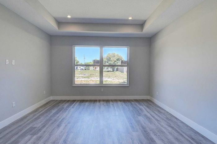 Bright and airy room with elegant laminate flooring, large window offering natural light and modern recessed lighting.