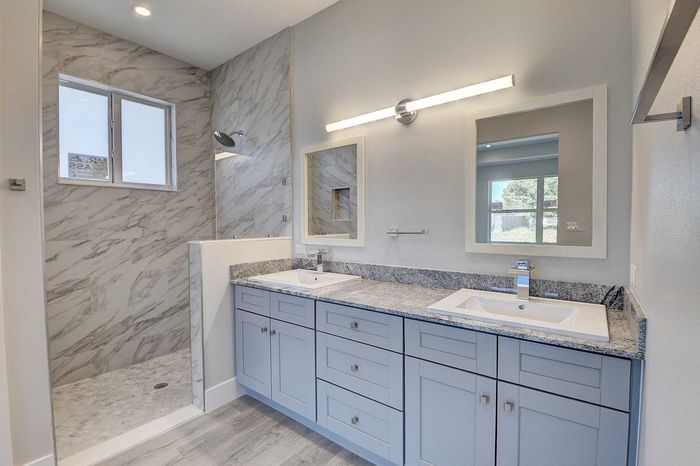 Elegant bathroom featuring dual sinks with granite countertops, modern mirrors, and a luxurious marble-tiled shower.