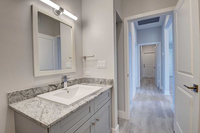 Modern bathroom with sleek granite countertop and elegant mirror, leading to a bright, spacious hallway.