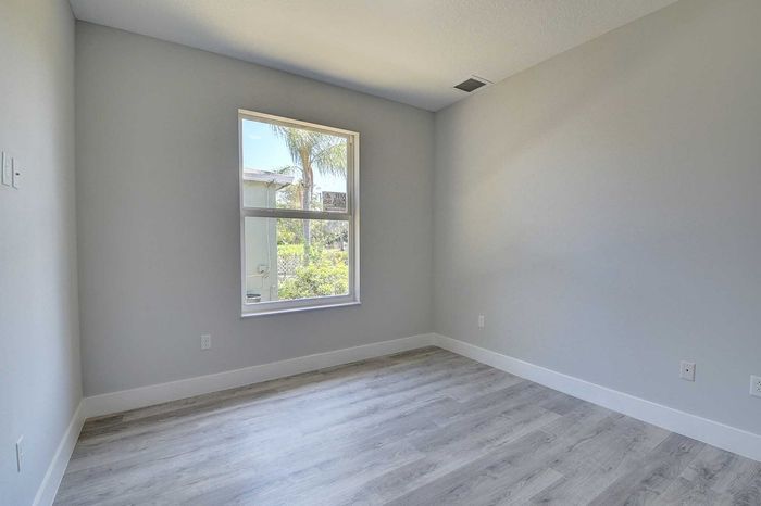 Bright, modern apartment room with large window, light gray walls, and elegant wood flooring.