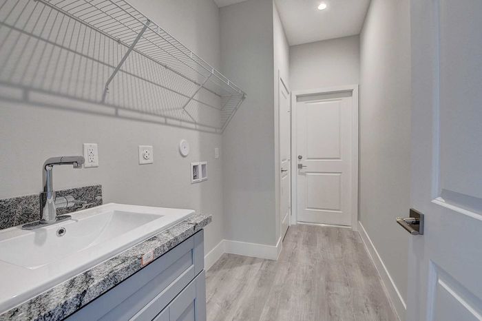 Modern laundry room with sleek granite countertop, spacious sink, and convenient shelving against a bright, contemporary design.