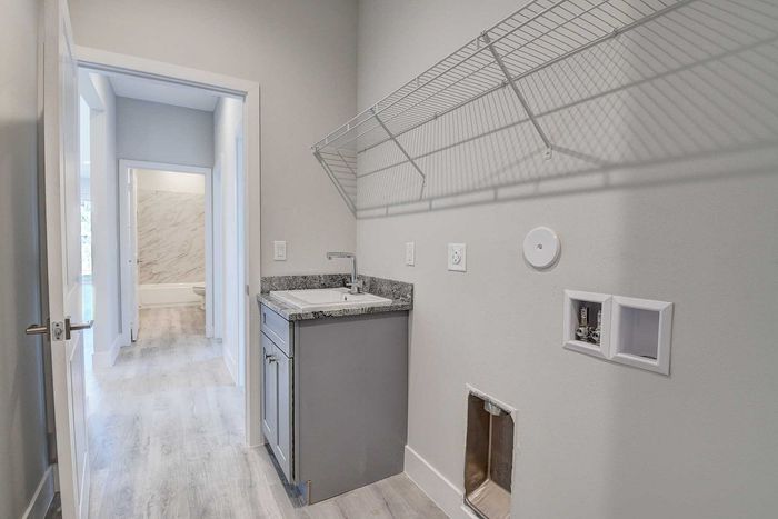 Bright and modern laundry room with chic light wood flooring, sleek granite countertop, and ample shelving space. Perfect blend of style and functionality.