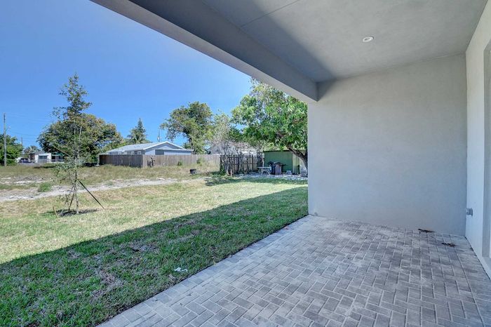 Inviting covered patio with paved floor opens to a spacious backyard, perfect for outdoor relaxation and entertainment.