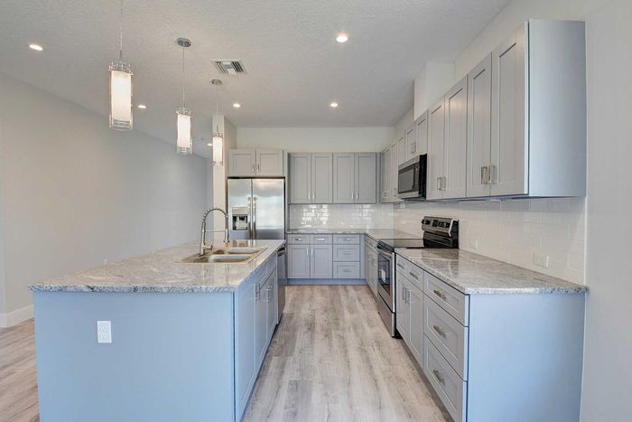 Sleek modern kitchen with elegant gray cabinetry, polished granite countertops, and stylish pendant lighting.