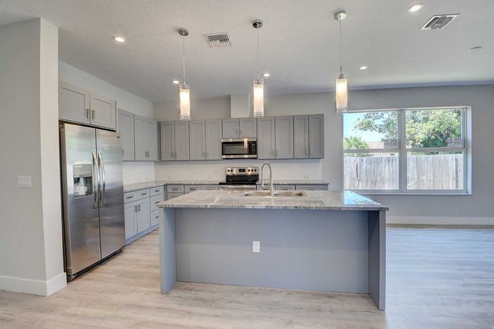 Contemporary kitchen with sleek gray cabinetry, stainless steel appliances, a marble countertop island, and modern pendant lighting.