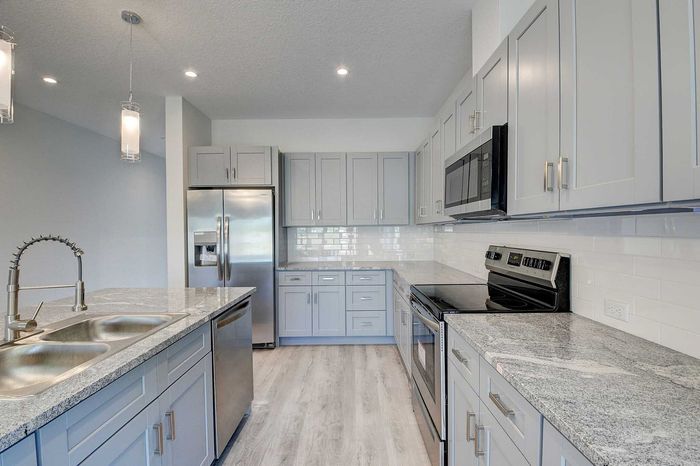 Modern kitchen with sleek gray cabinets, granite countertops, stainless steel appliances, and elegant pendant lighting.