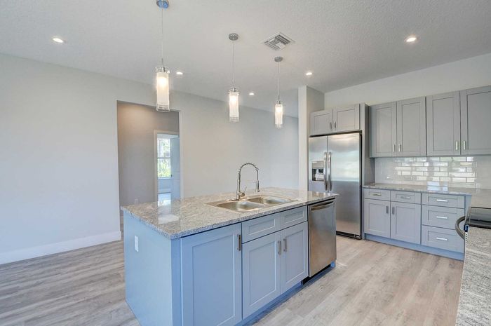 Modern kitchen with elegant gray cabinetry, granite countertops, and stainless steel appliances under chic pendant lighting.