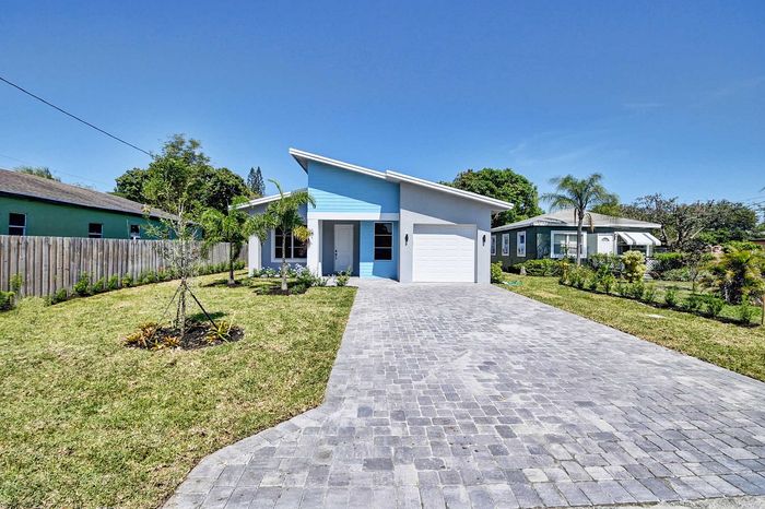 Charming modern house with a sleek blue and white exterior, single-car garage, and lush green lawn surrounded by tropical landscaping.
