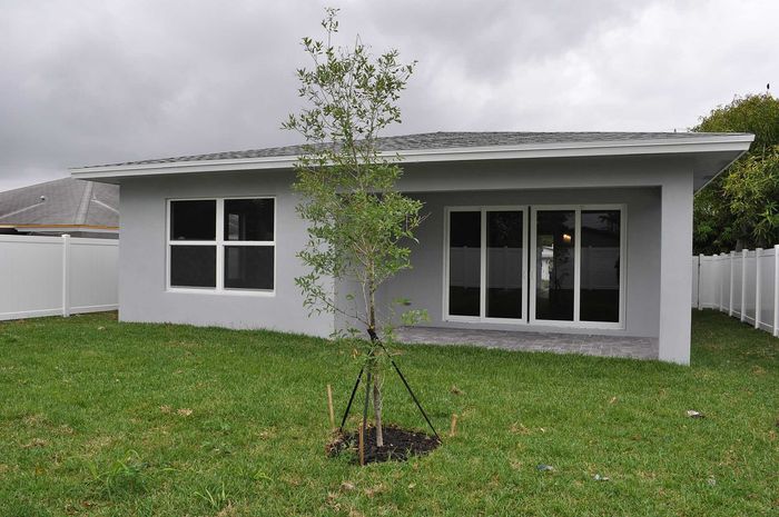 Charming modern home exterior with a lush green backyard and sleek patio doors, perfect for relaxation and outdoor gatherings.