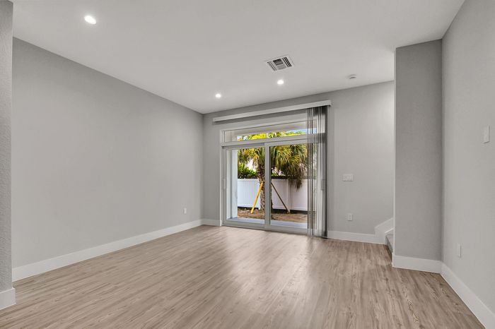 Bright living space with elegant wood flooring, large sliding glass doors, and lush outdoor views, perfect for a modern touch.