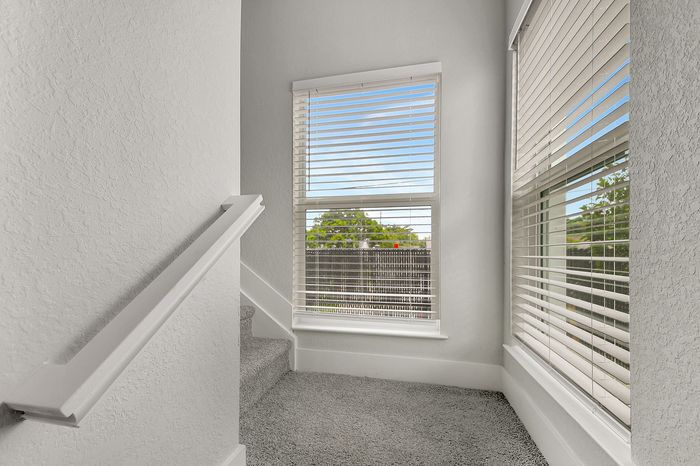 Bright and airy stairwell featuring modern carpeting and large windows with stylish blinds, offering a serene outdoor view.