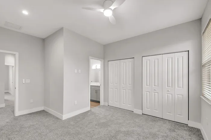 Modern bedroom with plush carpet, stylish ceiling fan, and ample closet space. Abundant natural light filters through large window blinds for a bright, inviting atmosphere.