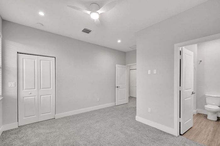 Bright, modern bedroom featuring plush carpeting, sleek ceiling fan, and en-suite bathroom access.