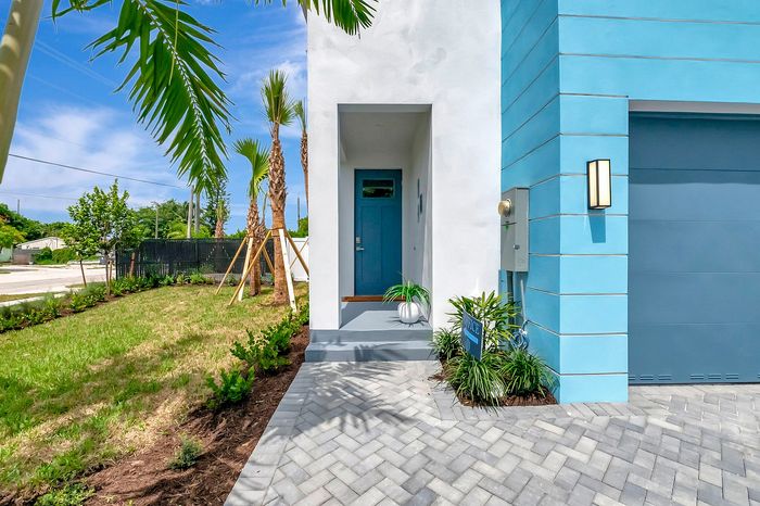 Striking modern home exterior with vibrant blue accents, lush palm trees, and a welcoming entryway.
