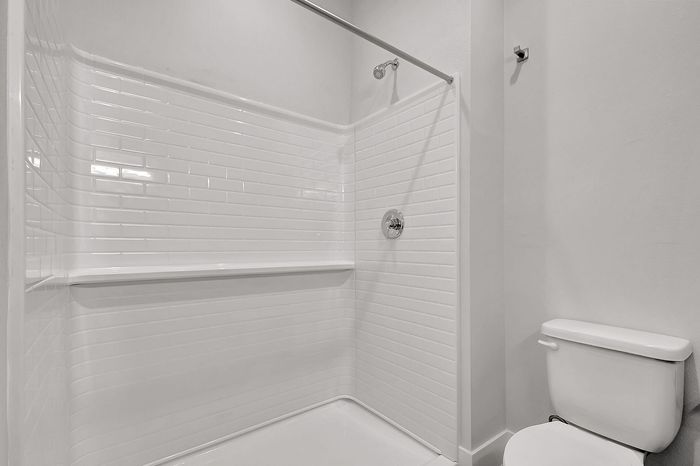 Contemporary bathroom featuring a sleek white shower with subway tile design and a pristine toilet, offering a clean and modern look.