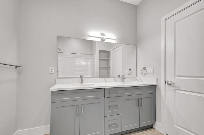 Elegant bathroom featuring dual sinks, sleek gray cabinetry, modern lighting, and a spacious mirror.