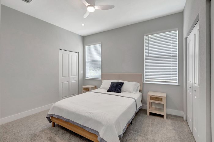 Bright and inviting bedroom with modern decor, featuring a comfortable double bed, cozy lighting, and ample natural light from two large windows.