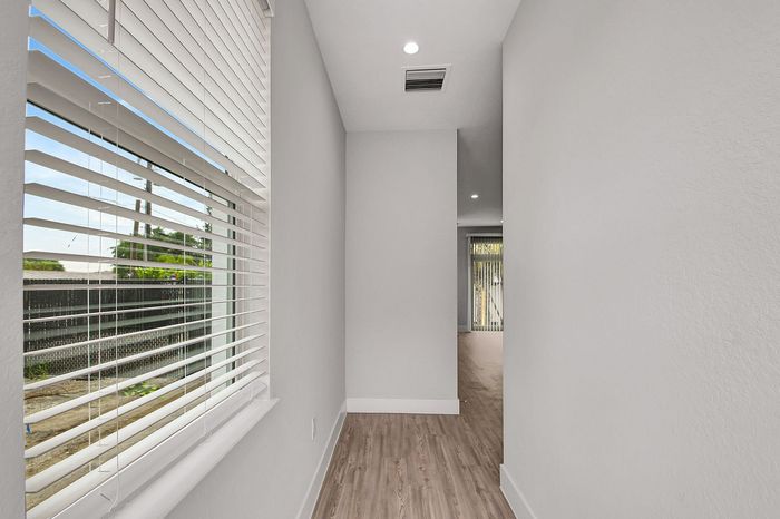 Bright hallway with stylish hardwood floors and large window blinds offering natural light.