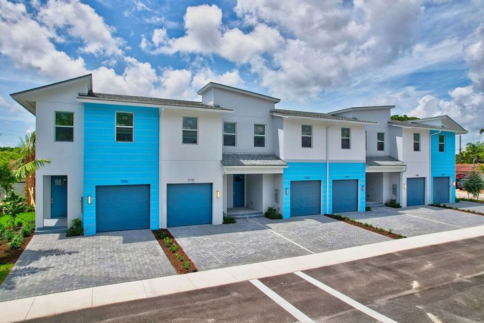 Modern townhouse row with vibrant blue accents and spacious driveways under a clear sky.