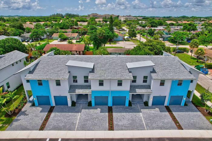Modern townhouses with vibrant blue accents and spacious driveways in a lush neighborhood.