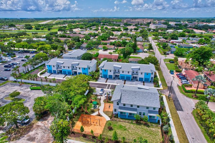 Vibrant aerial view showcasing modern blue and white apartment complex, surrounded by lush greenery and convenient access to nearby amenities.