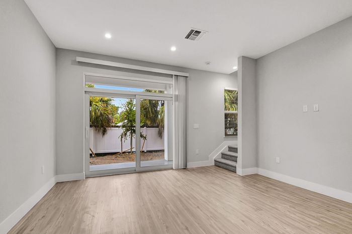 Modern living space with sleek hardwood flooring, large sliding glass doors opening to a private outdoor area, and a cozy carpeted staircase with natural light.