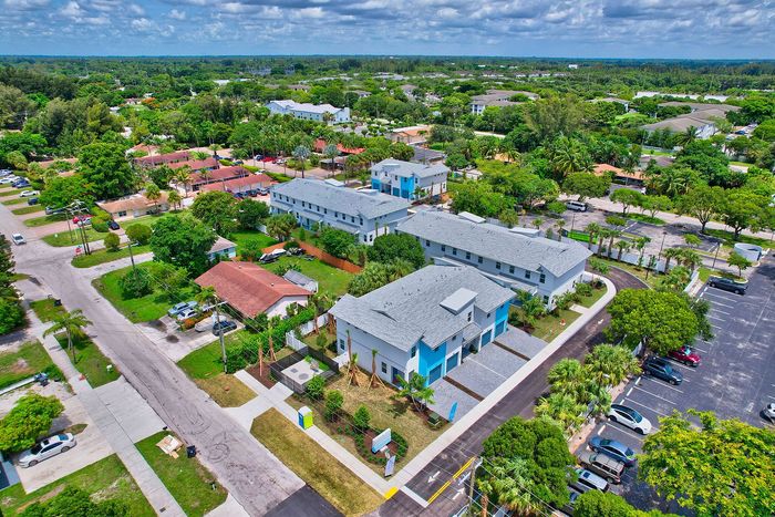 Vibrant aerial view of a modern apartment complex surrounded by lush greenery, showcasing convenient parking and unique blue accents in a thriving residential area.