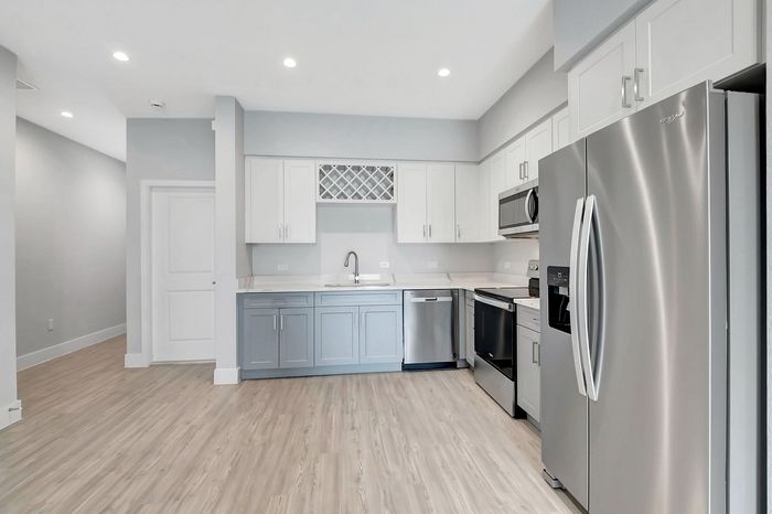 Modern kitchen featuring sleek stainless steel appliances, elegant white and gray cabinetry, and stylish hardwood flooring.