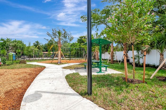 Charming community park with lush greenery, a winding path, and a vibrant picnic area under a bright blue sky.