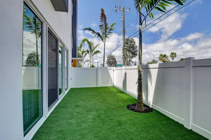 Charming outdoor space featuring lush artificial grass, elegant glass doors, and tall palm trees, perfect for relaxation and entertaining.
