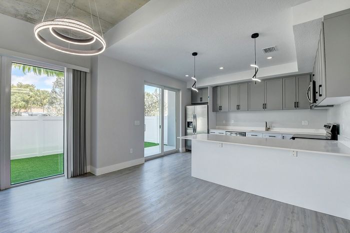 Modern open-plan kitchen and living area showcasing sleek gray cabinetry, contemporary lighting fixtures, and an inviting view to the outdoor space.