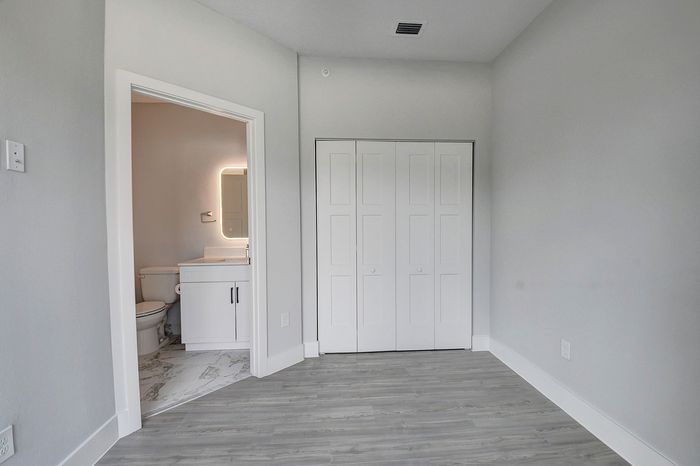 Modern minimalist bedroom featuring elegant hardwood floors, ample closet space, and an en-suite bathroom with contemporary finishes.
