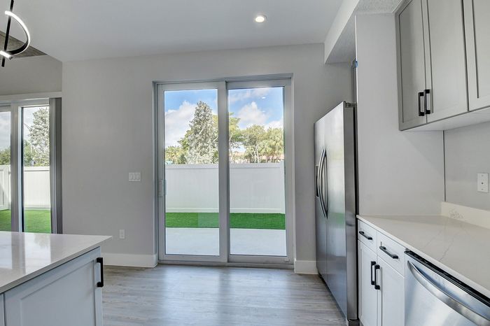 Modern kitchen with stainless steel appliances, white cabinetry, and large glass doors opening to a lush green backyard, offering a bright and inviting space.